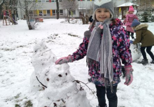 Dziewczynka stoi obok własnoręcznie ulepionego ze śniegu bałwana